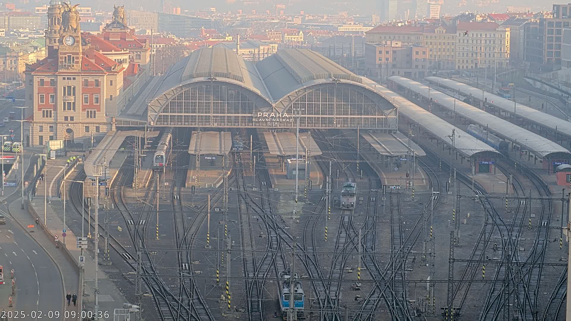 A large train station with numerous tracks and trains, under a hazy sky.