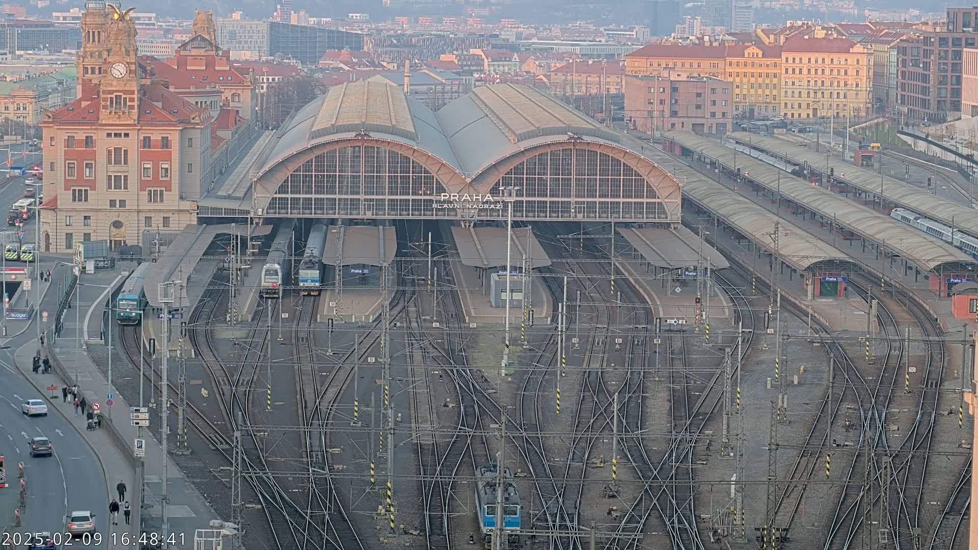 A large train station with many tracks and platforms, surrounded by city buildings, under a mostly clear sky.