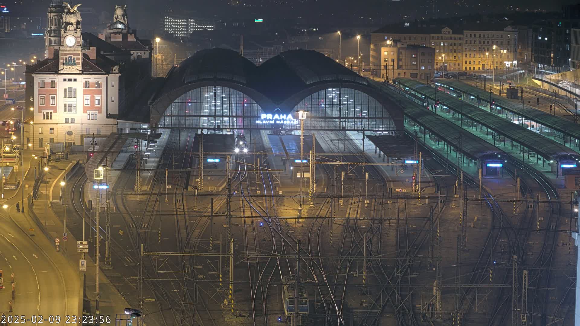 A nighttime, high-angle view of a large, illuminated train station with numerous tracks and platforms.