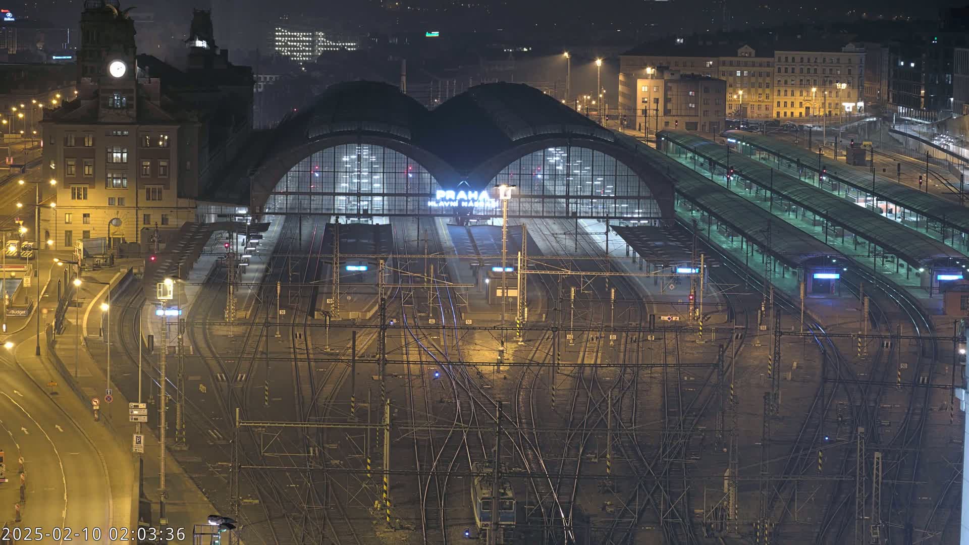 A nighttime aerial view of a large, illuminated train station with numerous tracks and platforms.
