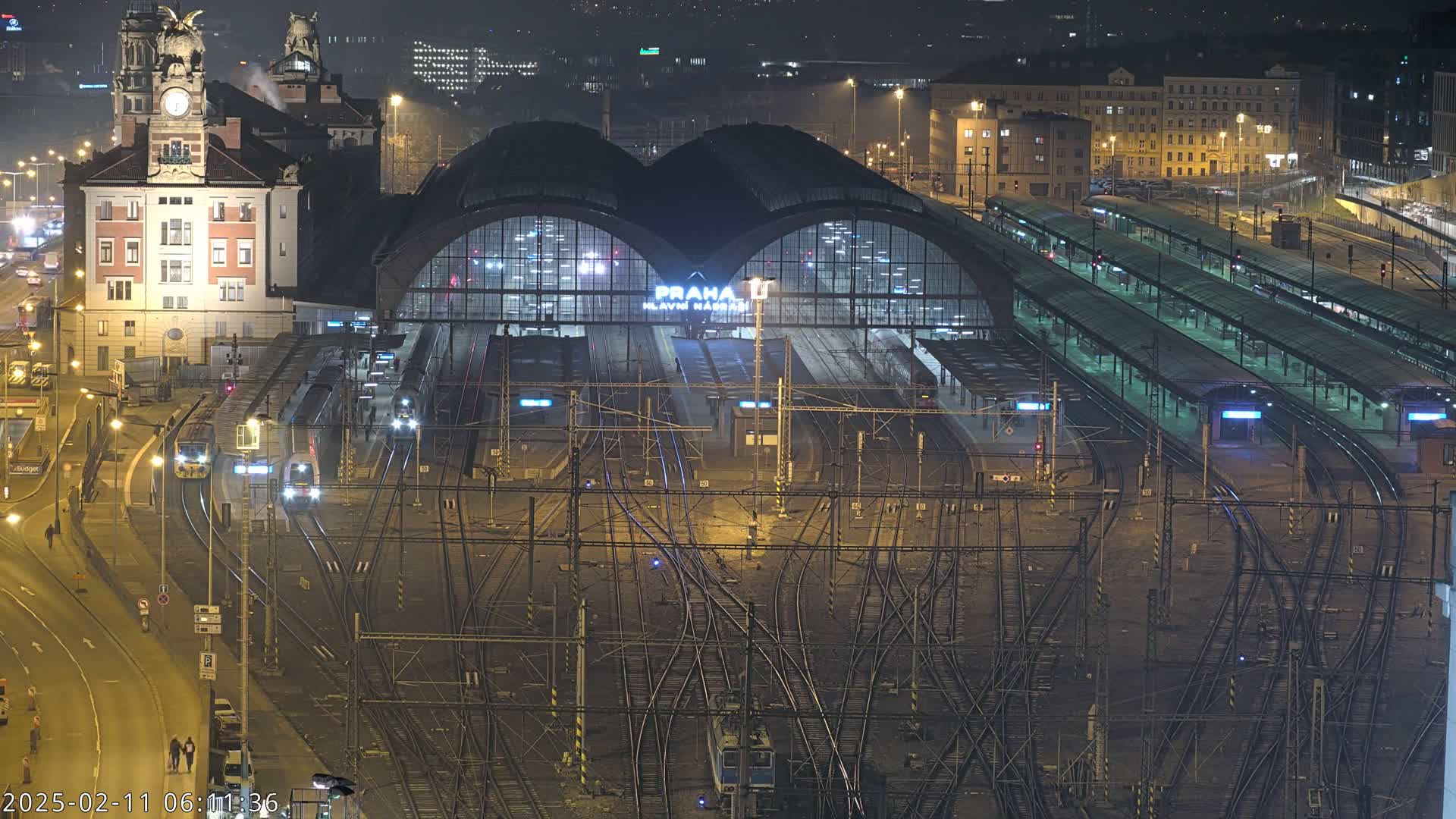 A nighttime aerial view of a busy train station with numerous tracks and platforms, illuminated by streetlights.