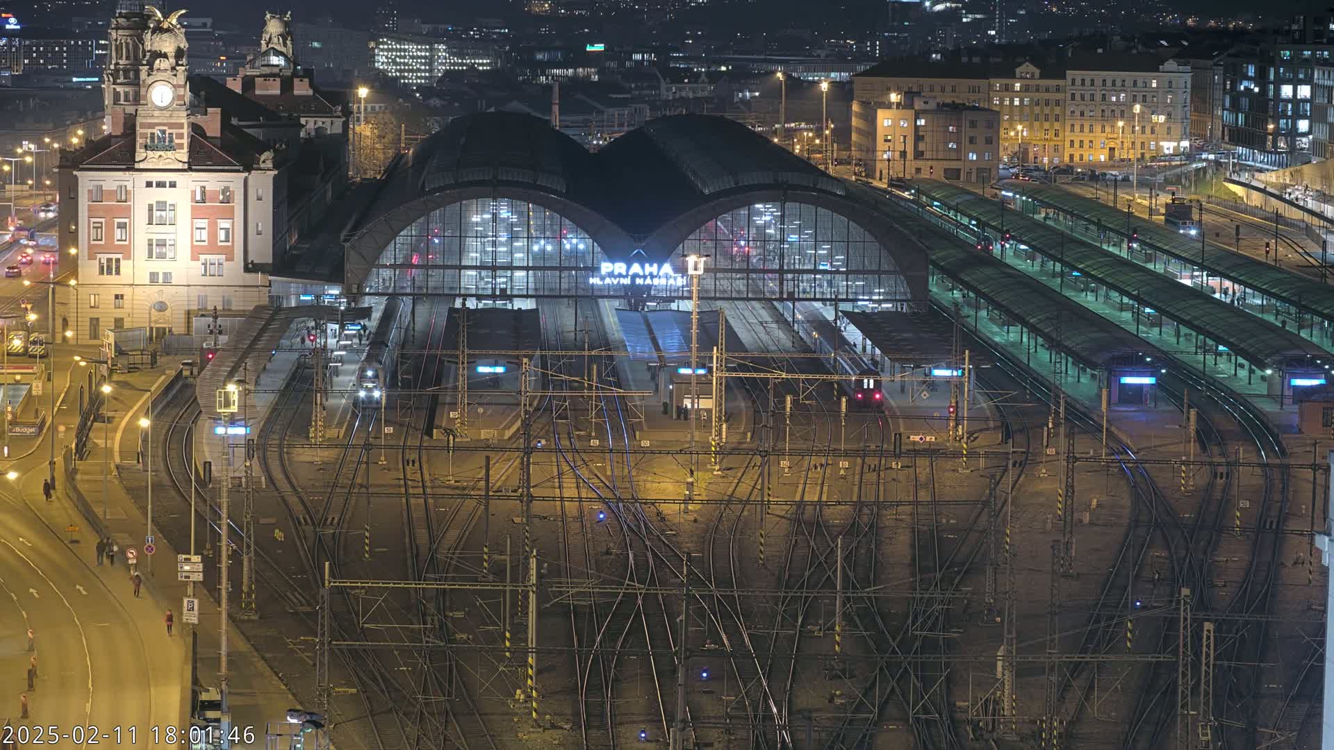 A nighttime aerial view of a large train station with numerous tracks and platforms, illuminated by artificial lights.