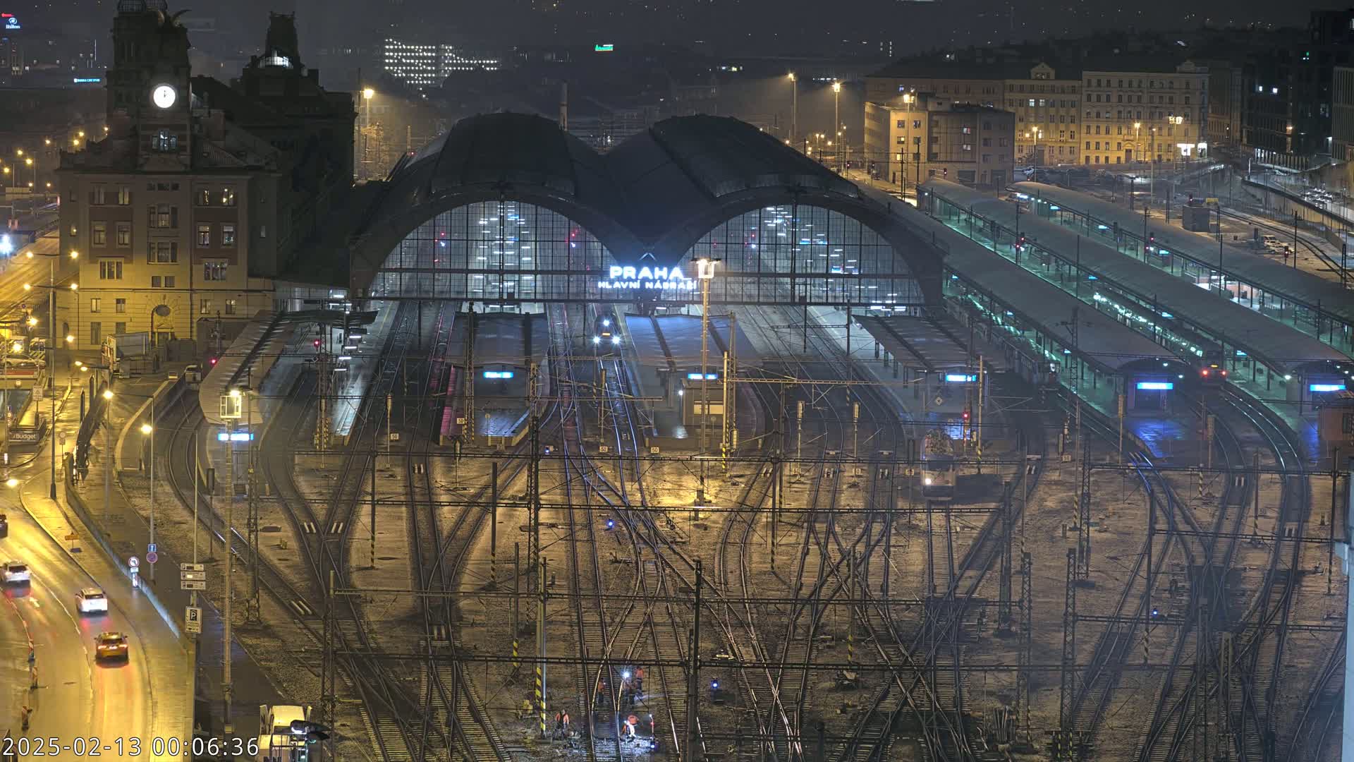 A nighttime aerial view of a large, busy train station with numerous tracks and platforms, illuminated by artificial lights under a dark sky.