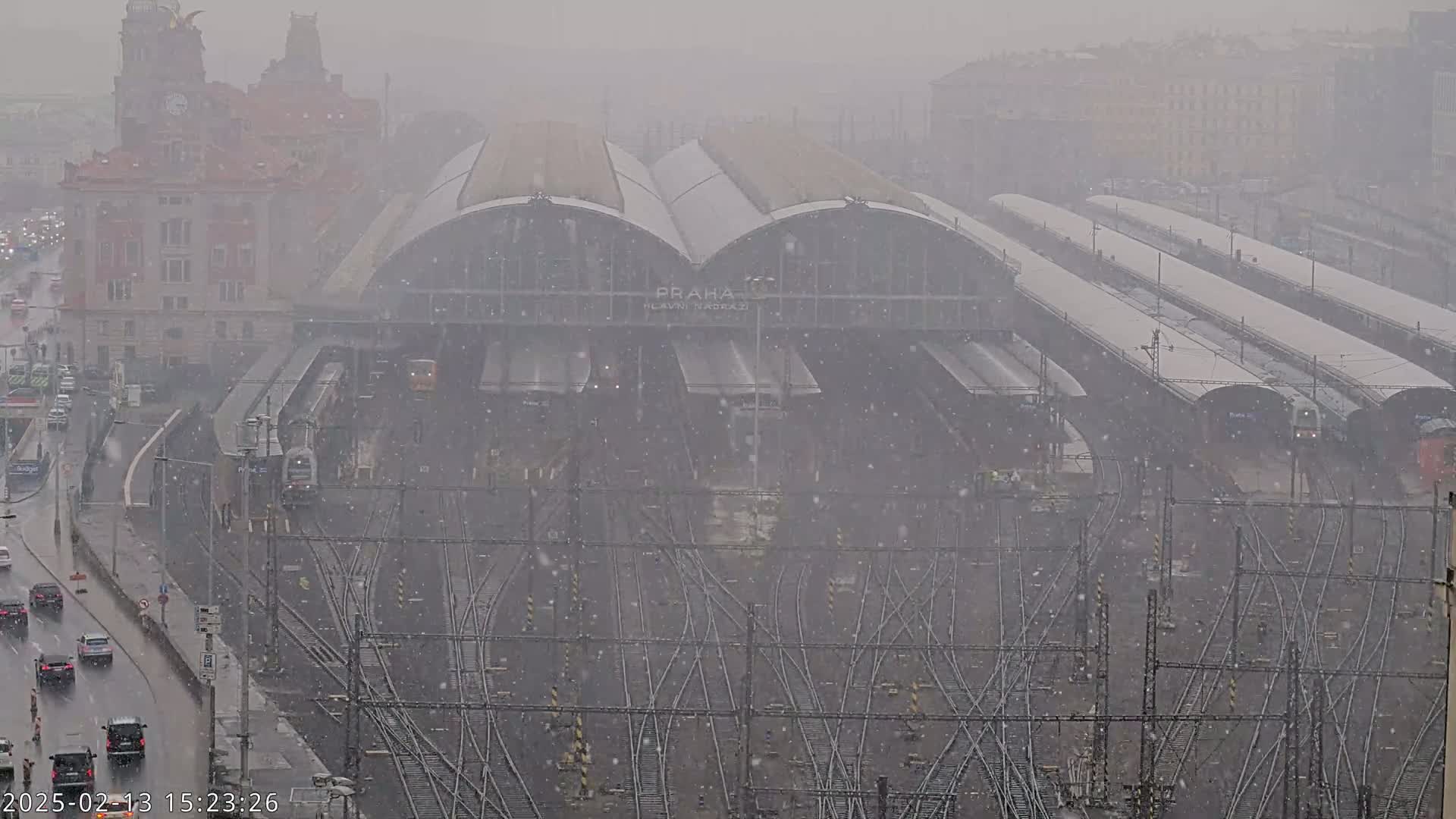 A large train station with many tracks and trains is seen under heavy snowfall.