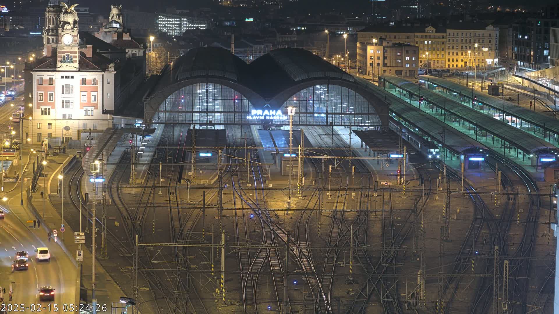 A large, illuminated train station at night, with many tracks and platforms, surrounded by city buildings.