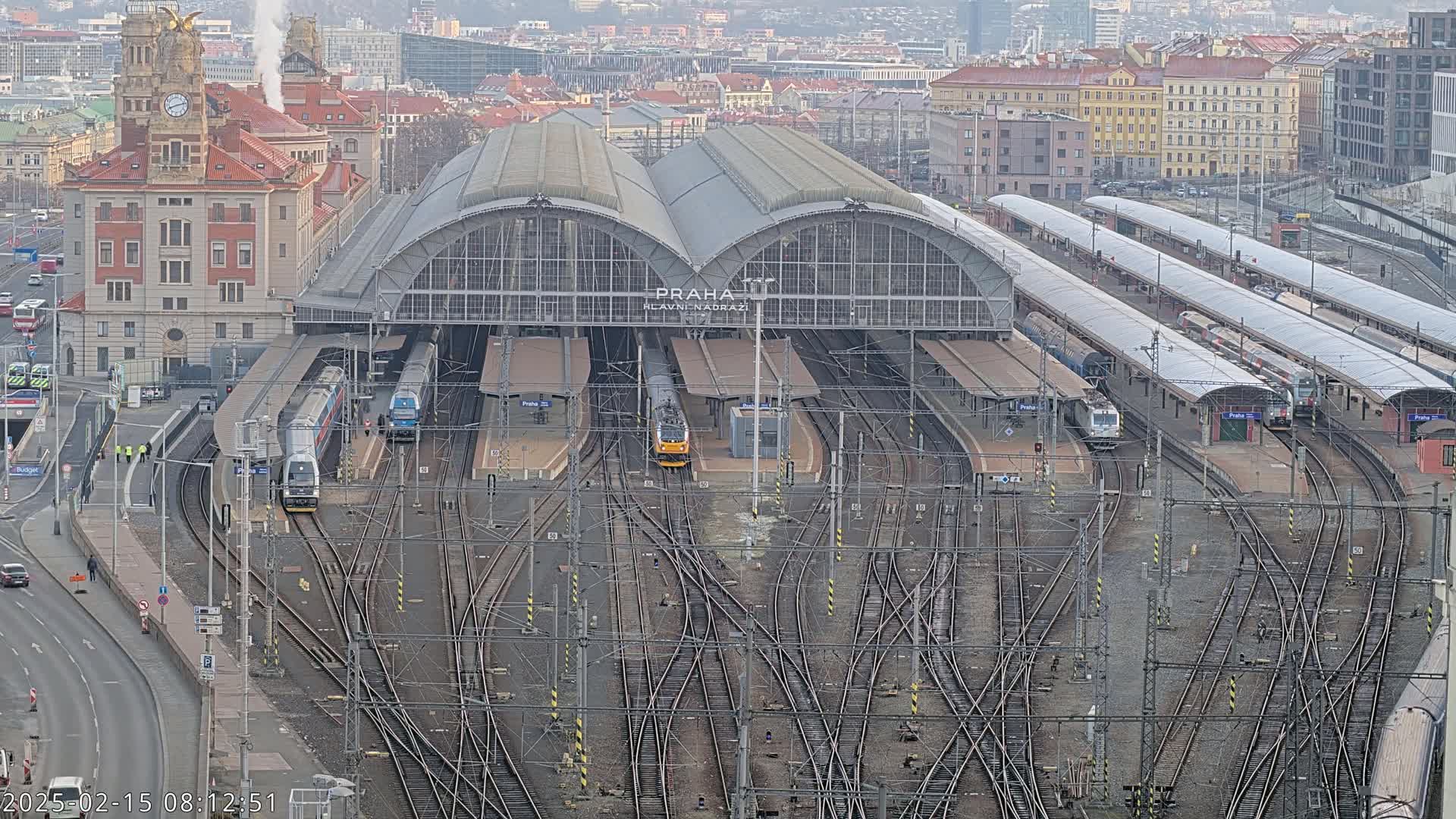 A large train station with multiple tracks and several trains, under a cloudy sky.