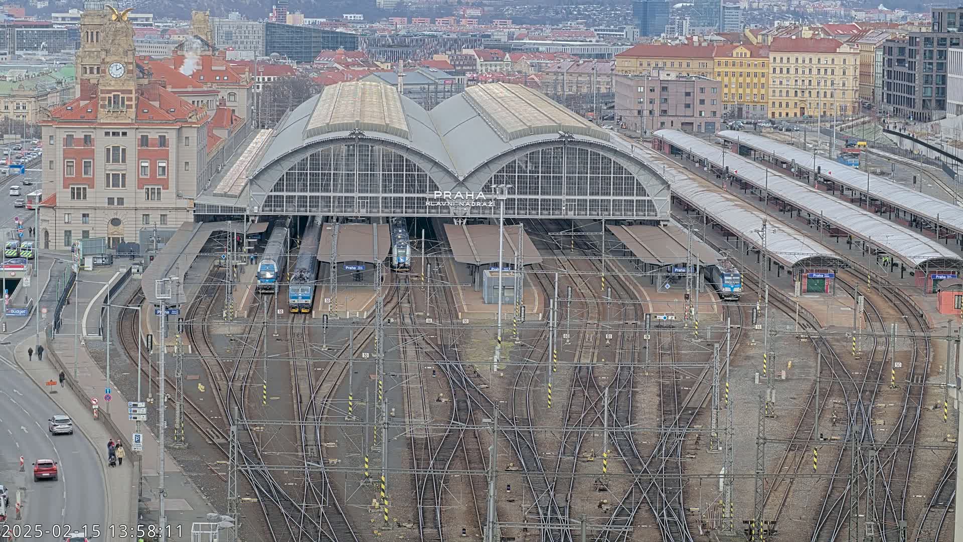 An aerial view shows a large train station with multiple tracks and several trains, under an overcast sky.