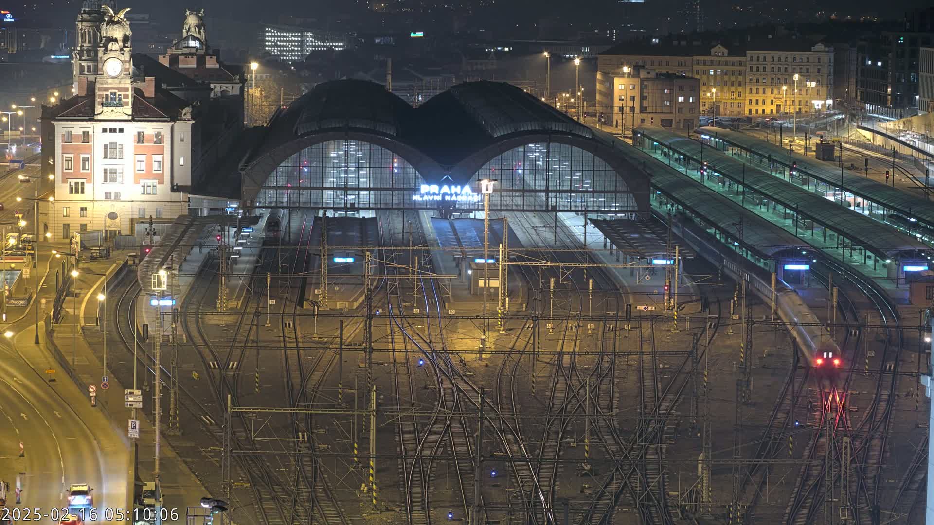 A nighttime, high-angle view of a busy train station with many tracks and platforms, illuminated by artificial light.