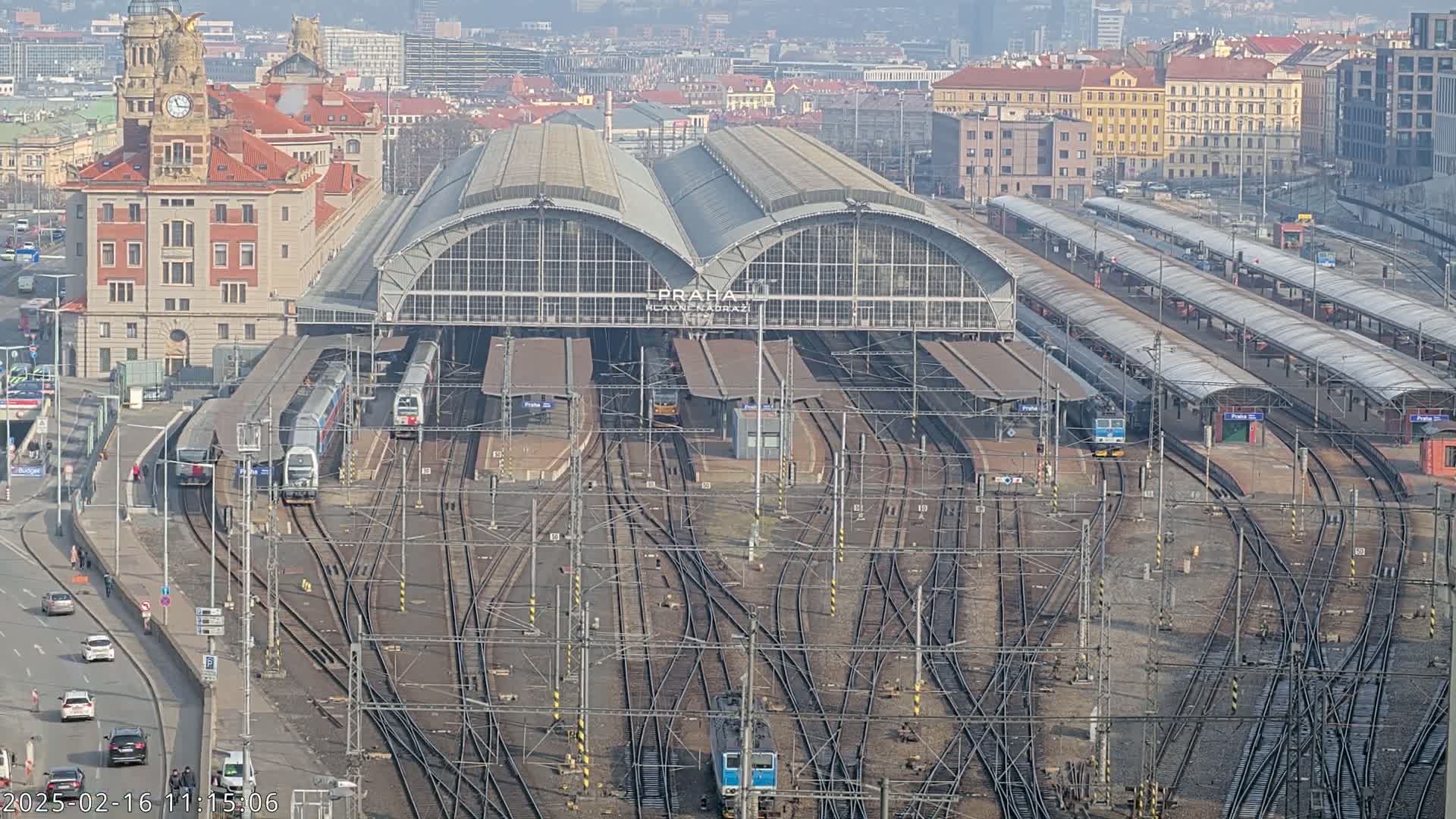 A large train station with numerous tracks and trains, situated in a city on a clear, sunny day.
