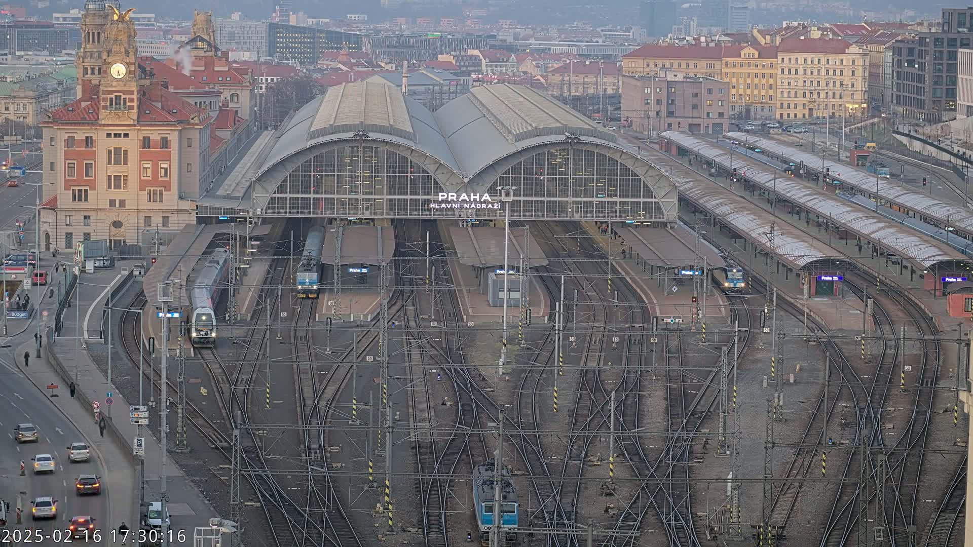 A large train station with numerous tracks and trains, surrounded by city buildings, on an overcast day.