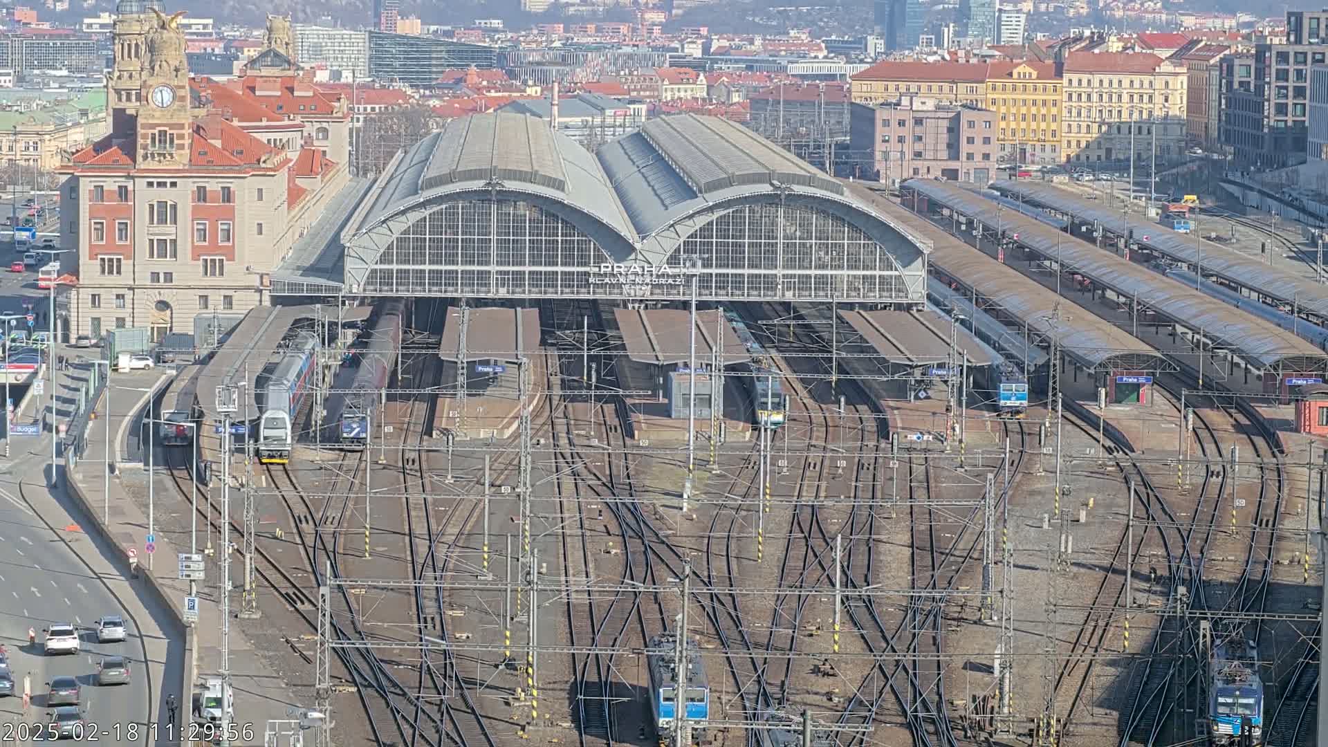 A large train station with numerous tracks and trains, situated in a city on a sunny day.