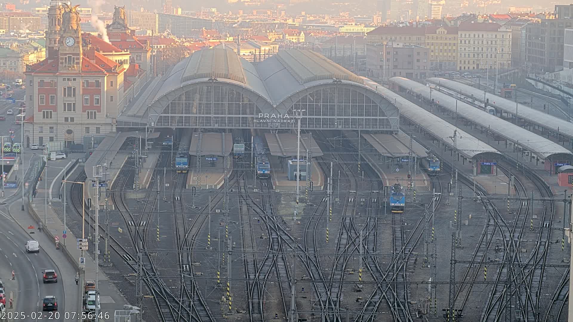 A large train station with numerous tracks and several trains, situated in a city on a hazy day.