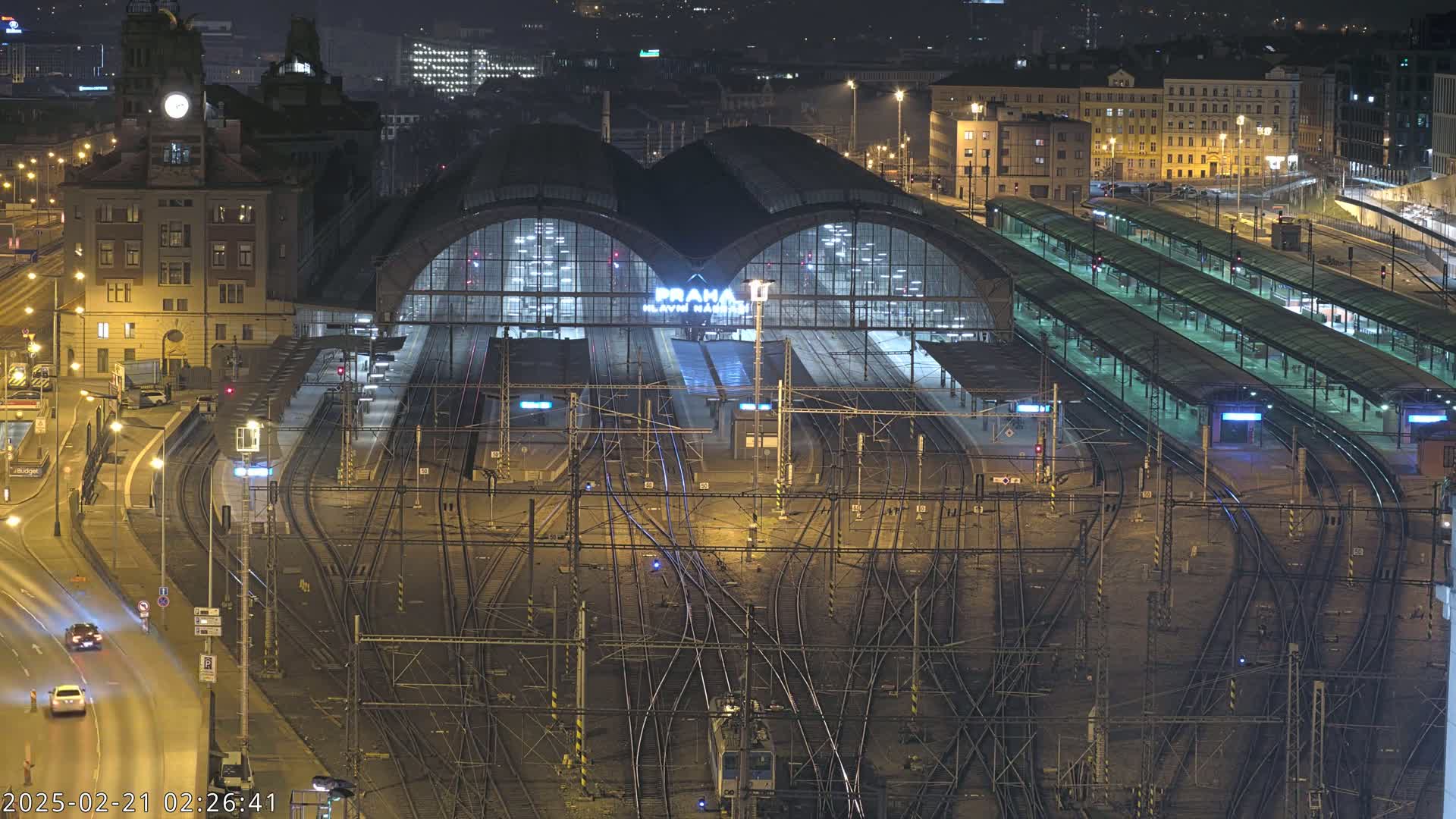 A brightly lit train station at night with numerous tracks and platforms, surrounded by city buildings.