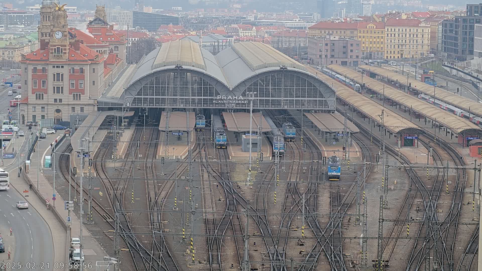 A large train station with numerous tracks and trains, surrounded by city buildings, on a cloudy day.
