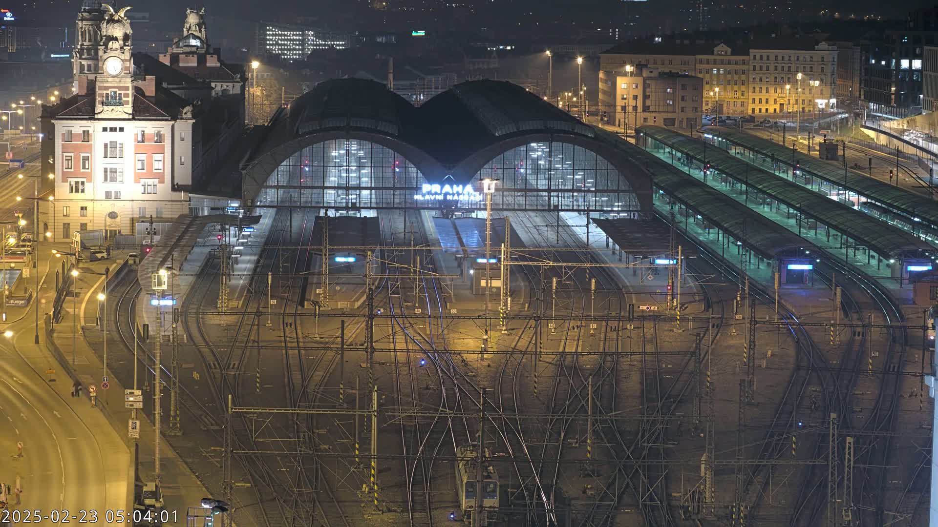 A large, illuminated train station at night, with many tracks and platforms, and a large building in the foreground.