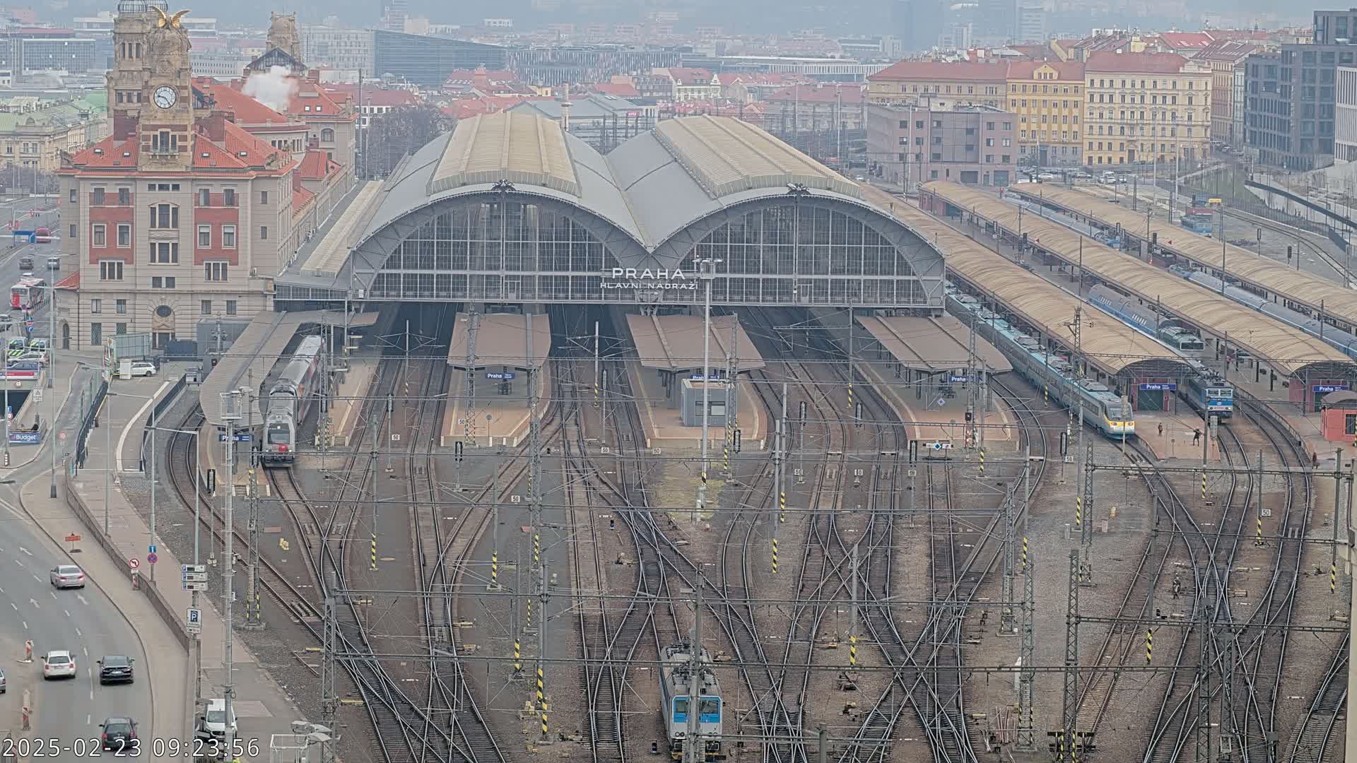 A large train station with numerous tracks and several trains, viewed from above on an overcast day.