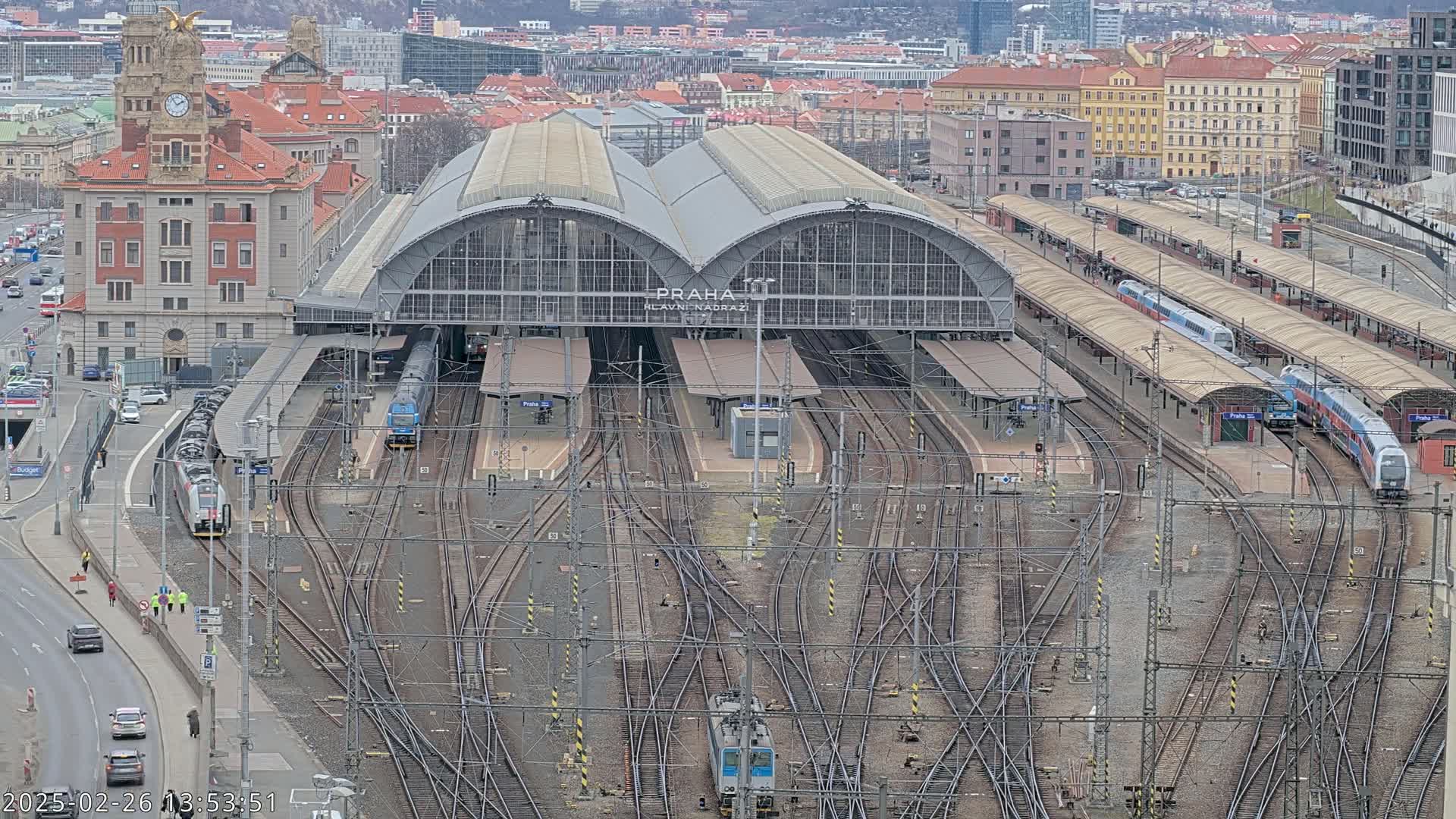 A large train station with numerous tracks and trains, situated in a city on an overcast day.