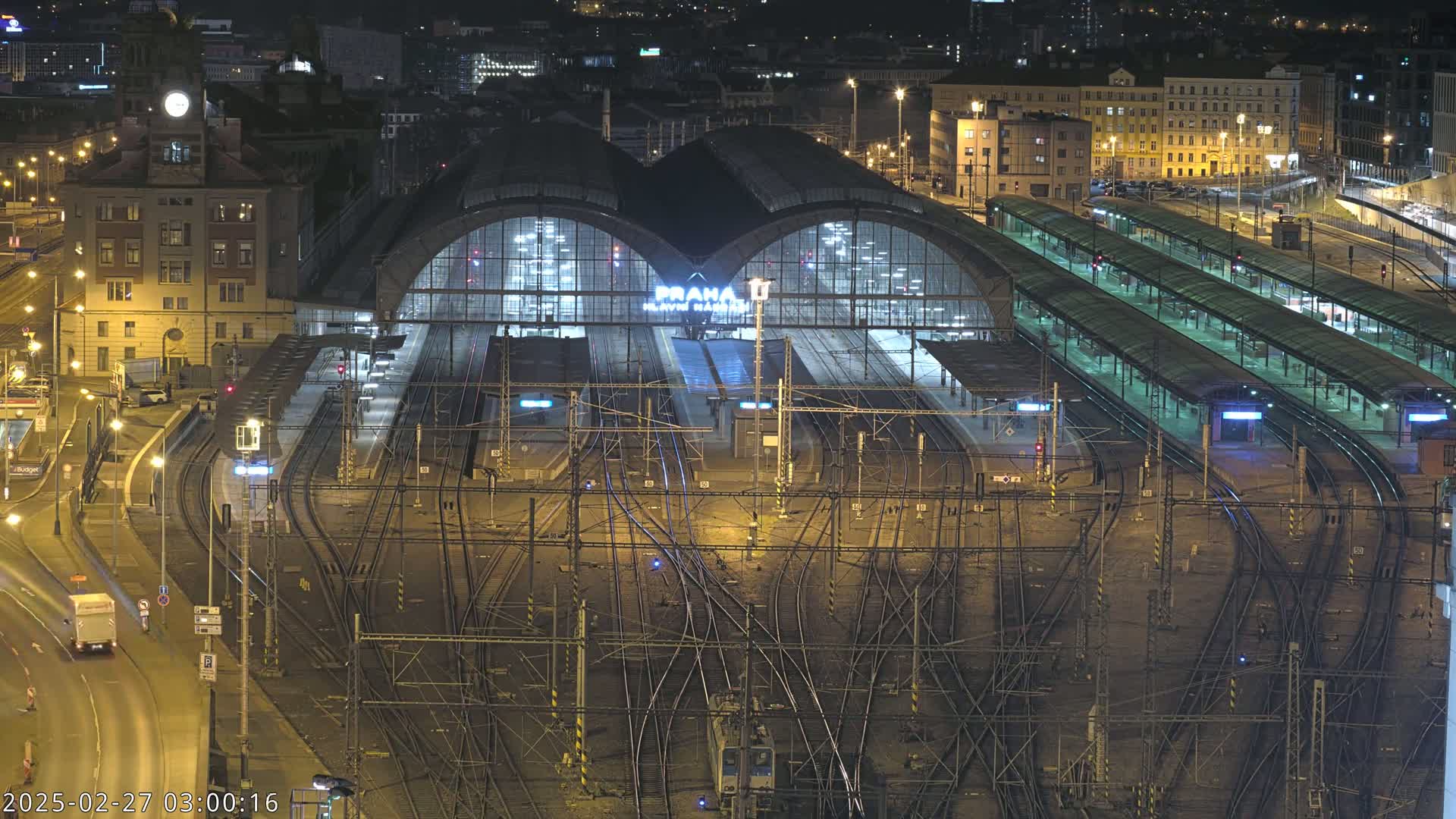 A nighttime, high-angle view of a large, illuminated train station with numerous tracks and platforms.