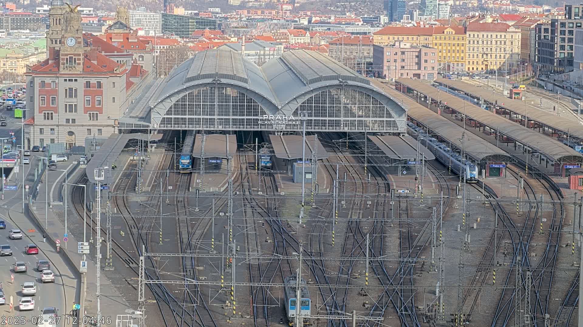 A large train station with numerous tracks and trains under a sunny sky.