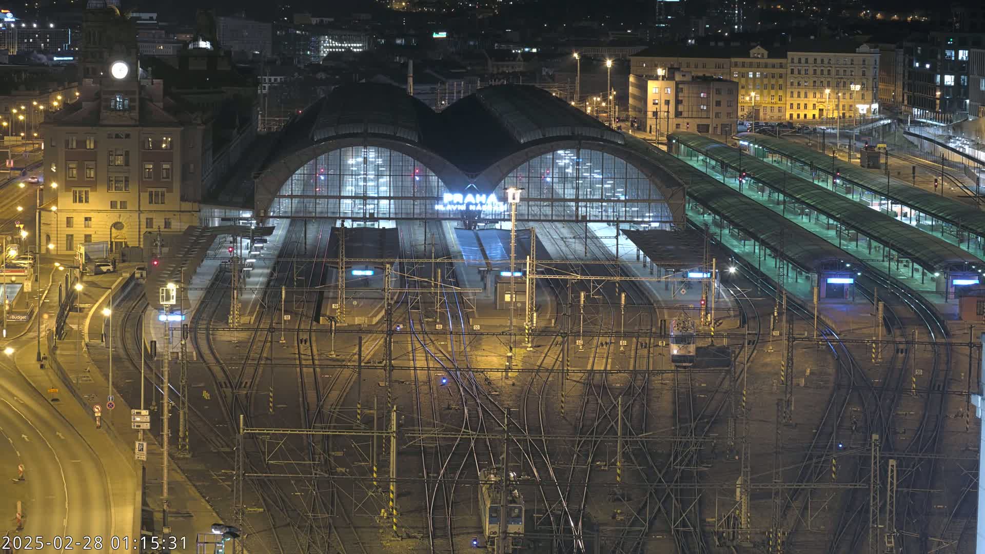A large, illuminated train station at night, surrounded by a complex network of train tracks and platforms.