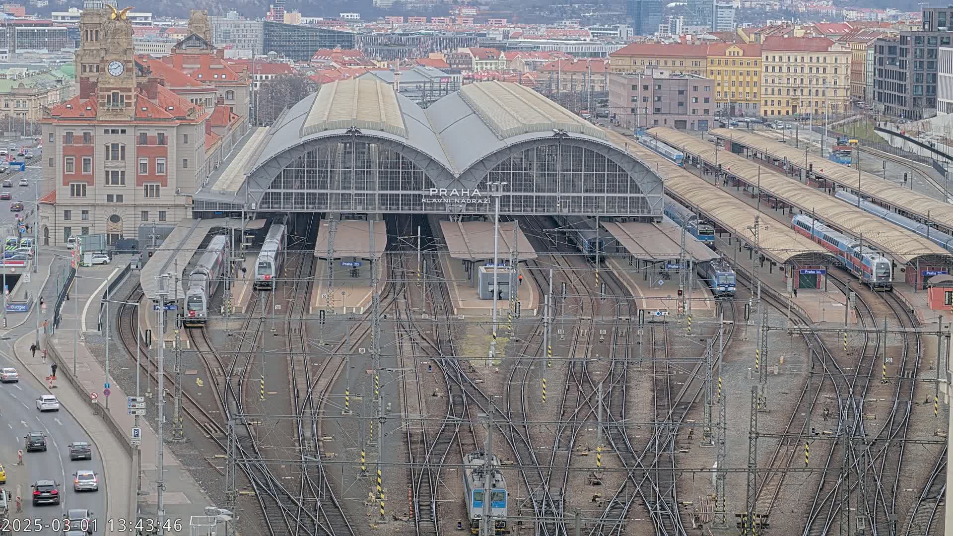 A large train station with numerous tracks and trains, surrounded by city buildings under an overcast sky.