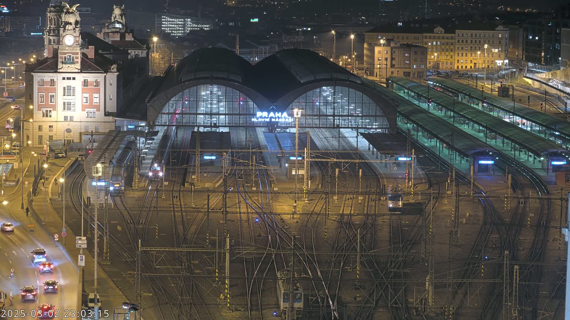 A nighttime, high-angle view of a busy train station with numerous tracks and platforms, illuminated by artificial lights.