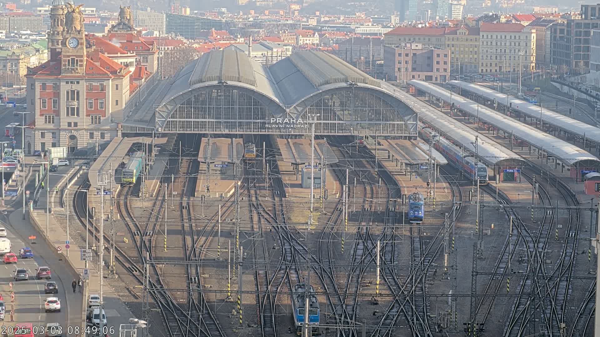 A large train station with numerous tracks and trains, viewed from above on a clear, sunny day.