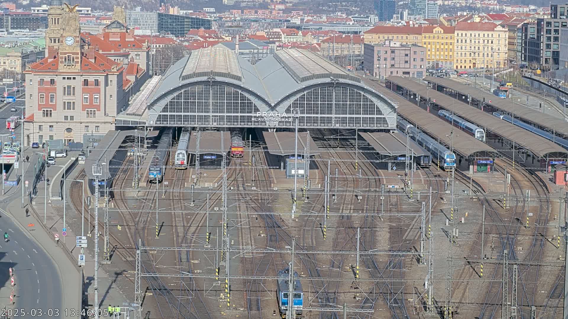A large train station with numerous tracks and trains, under a clear sky.