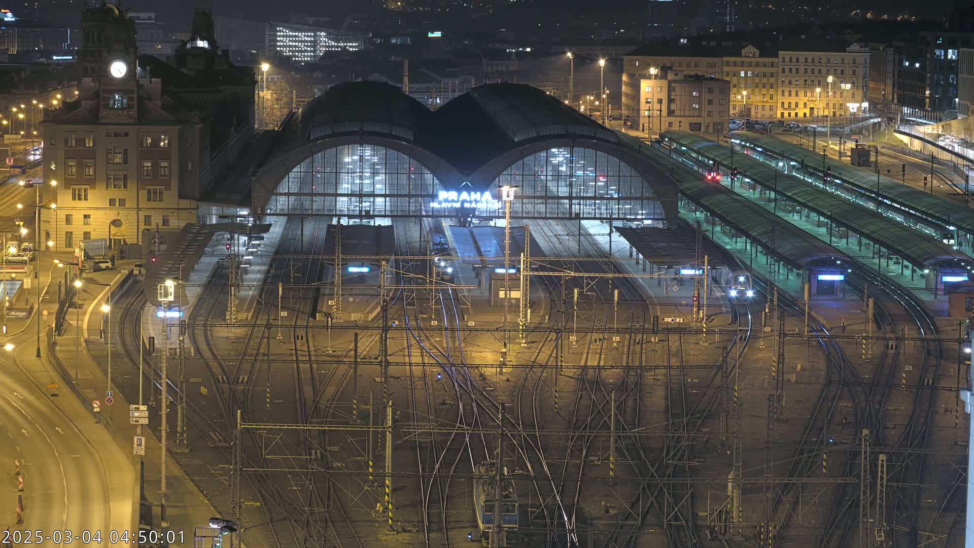 A nighttime, aerial view of a large, illuminated train station with numerous tracks and platforms.