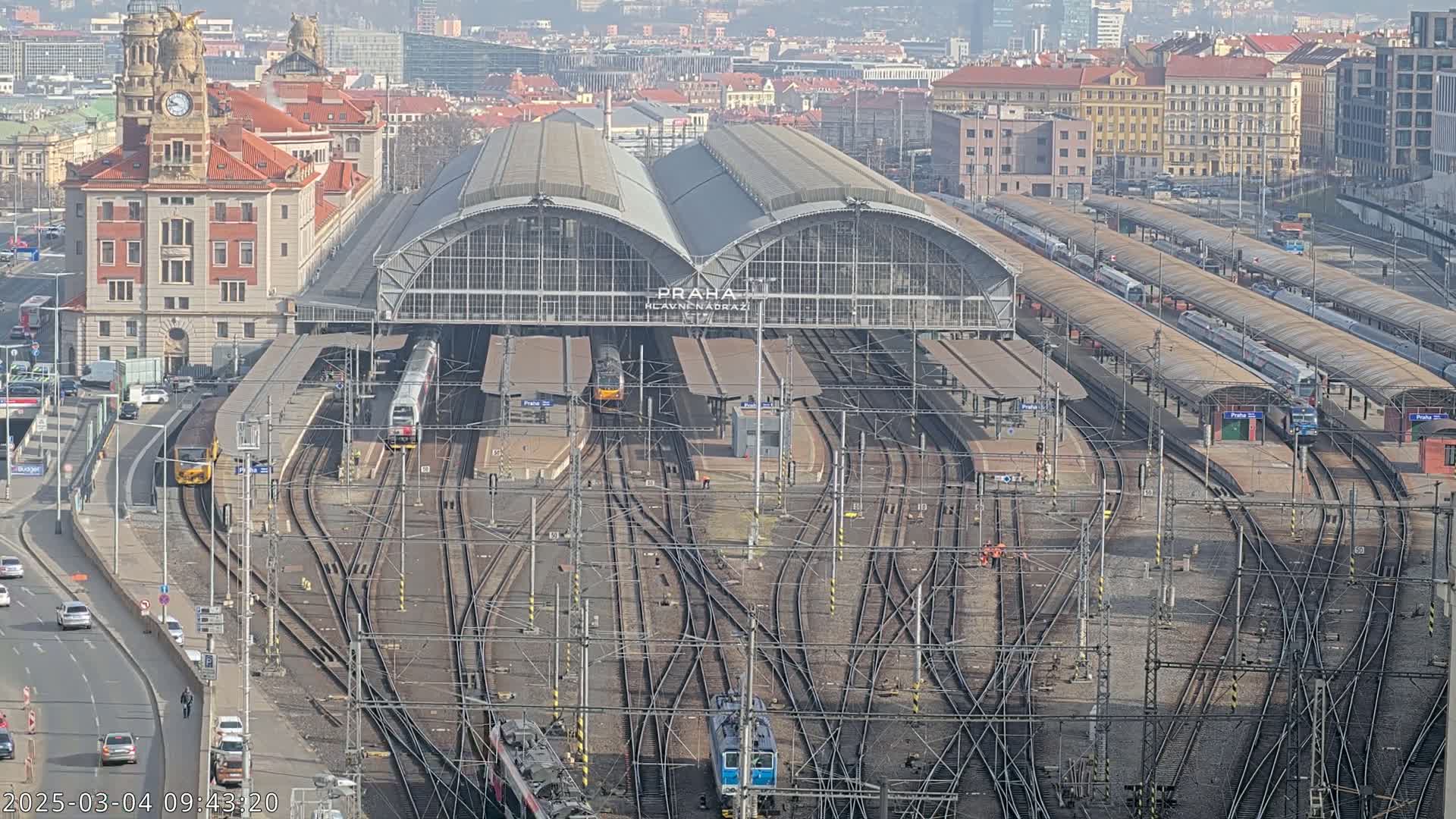 A large train station with numerous tracks and trains, under a clear, sunny sky.