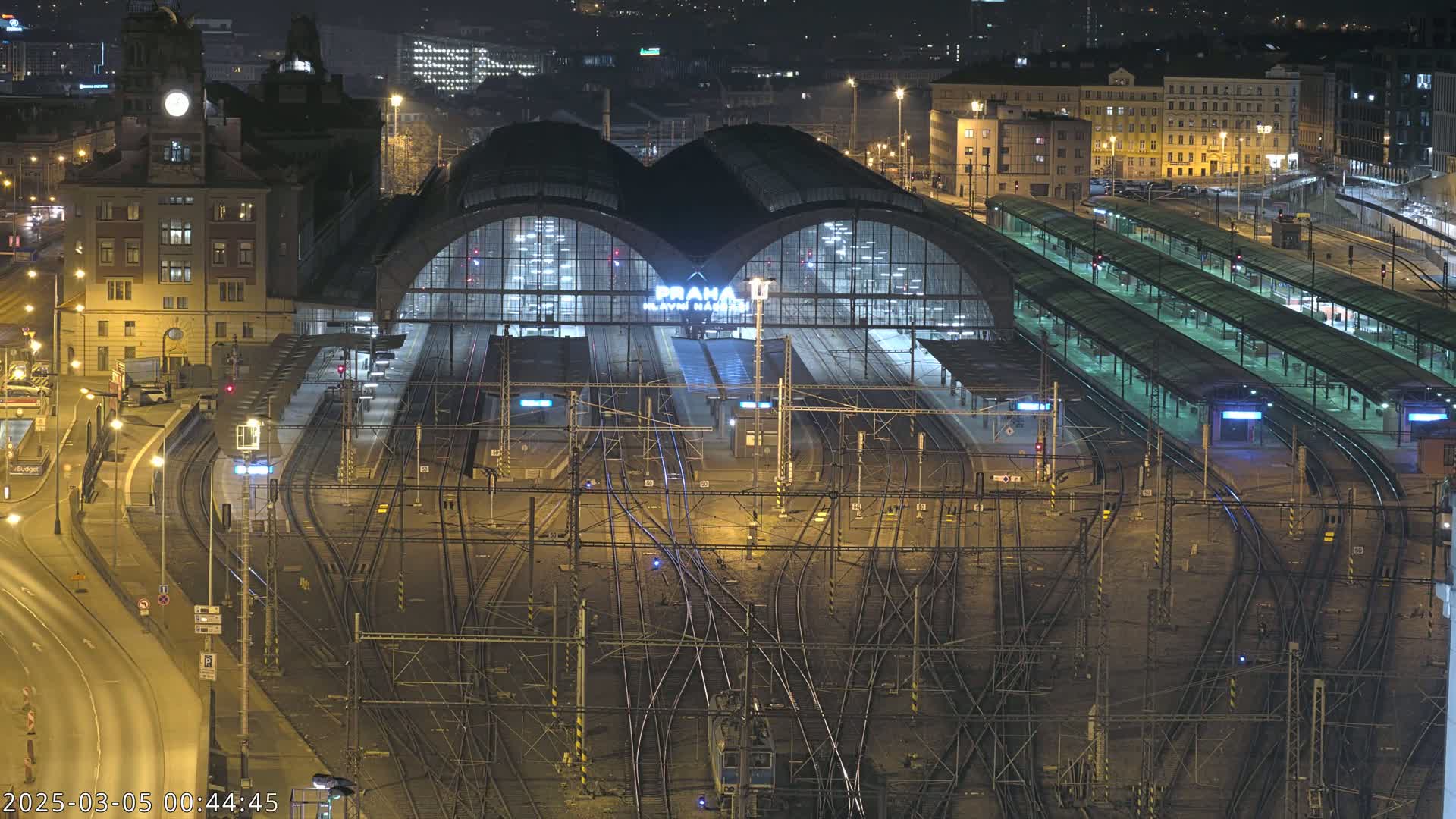 A nighttime aerial view of a large, illuminated train station with many tracks and platforms.