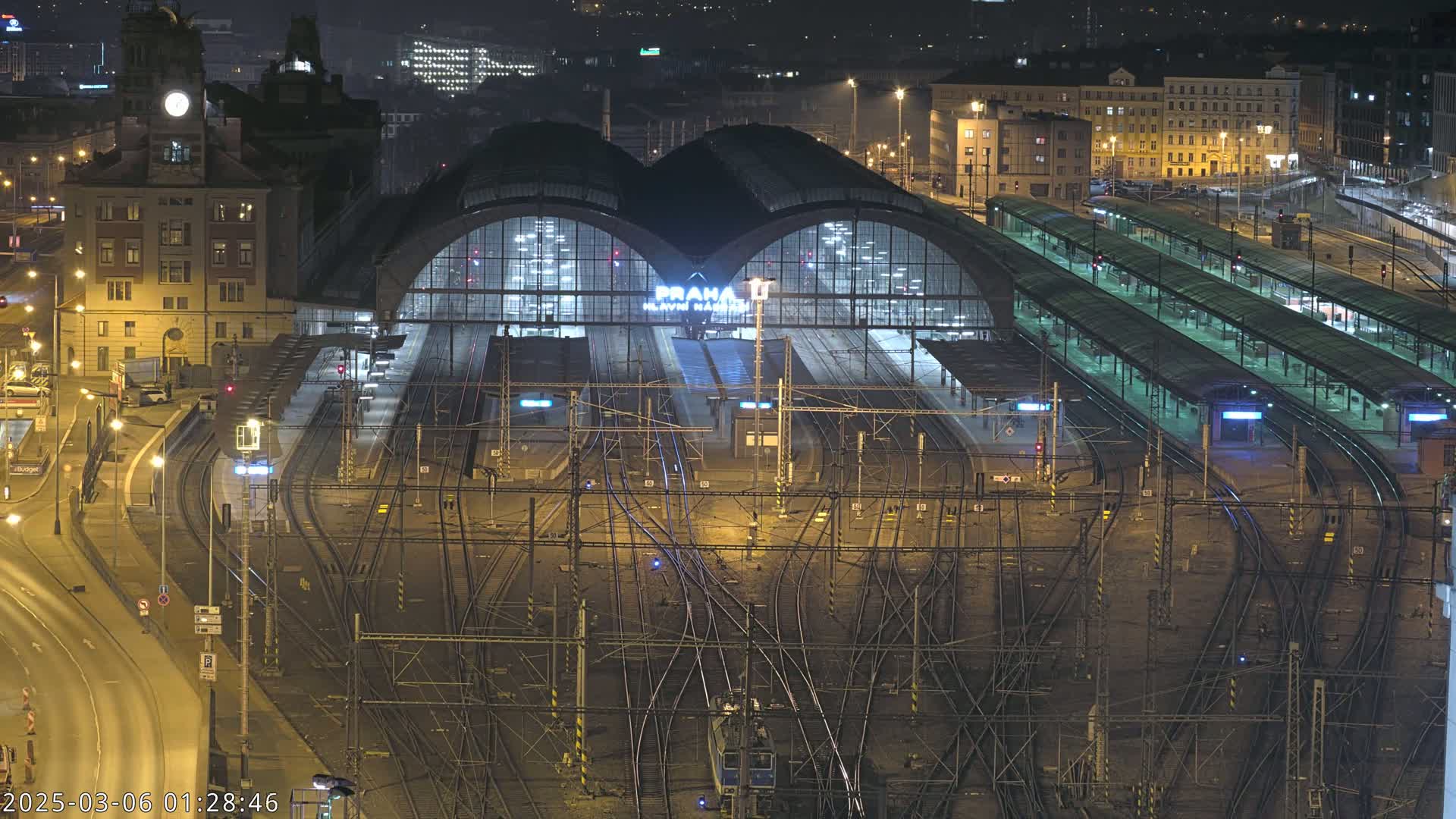A nighttime aerial view of a large, illuminated train station with numerous tracks and platforms.