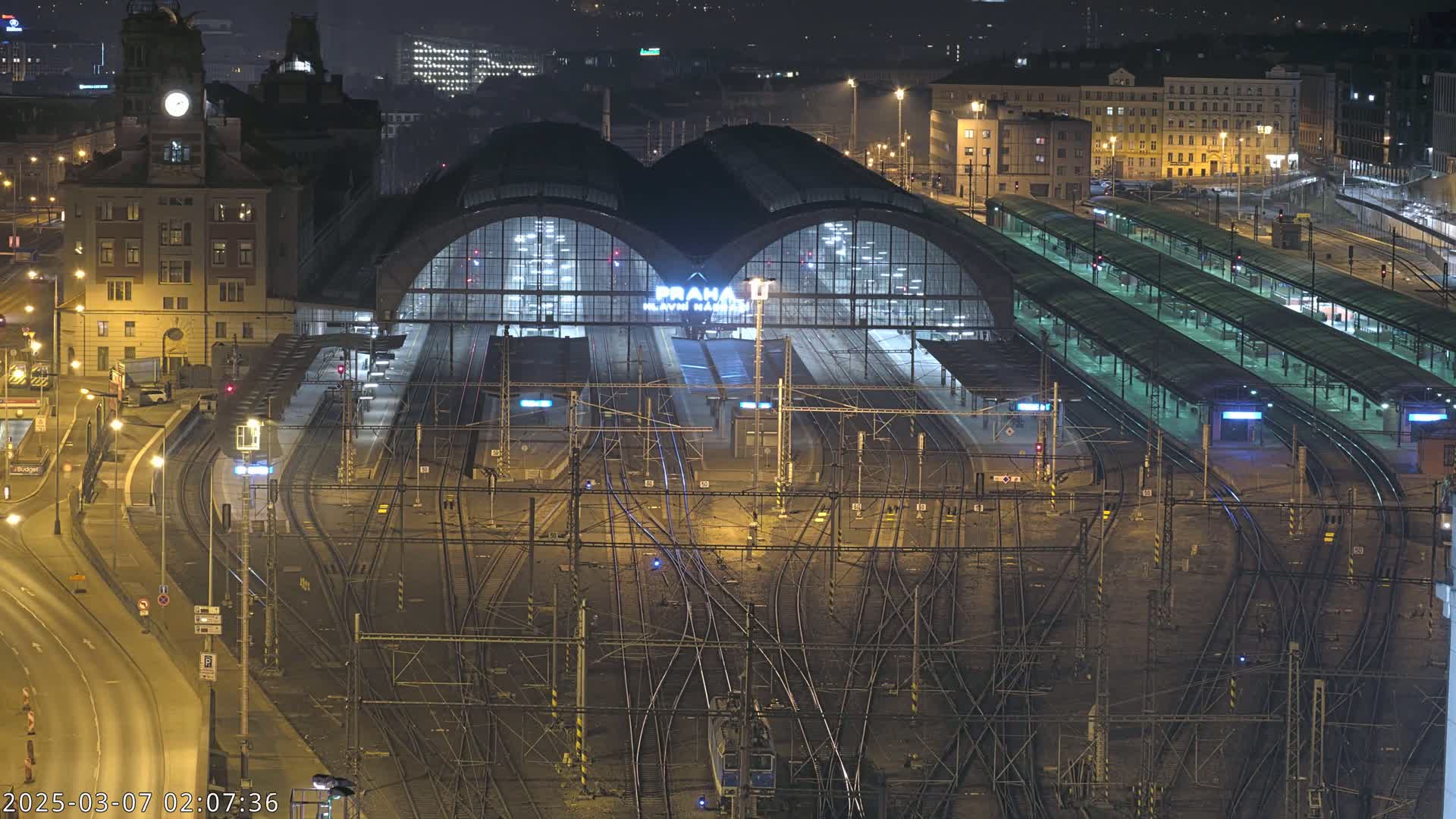 A large, illuminated train station at night with a complex network of train tracks surrounding it.