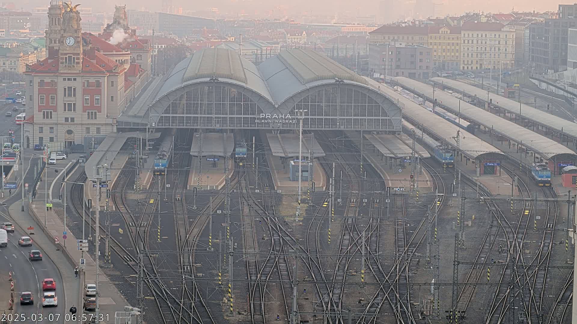 A large train station with numerous tracks and trains, situated in a city on a hazy or foggy day.