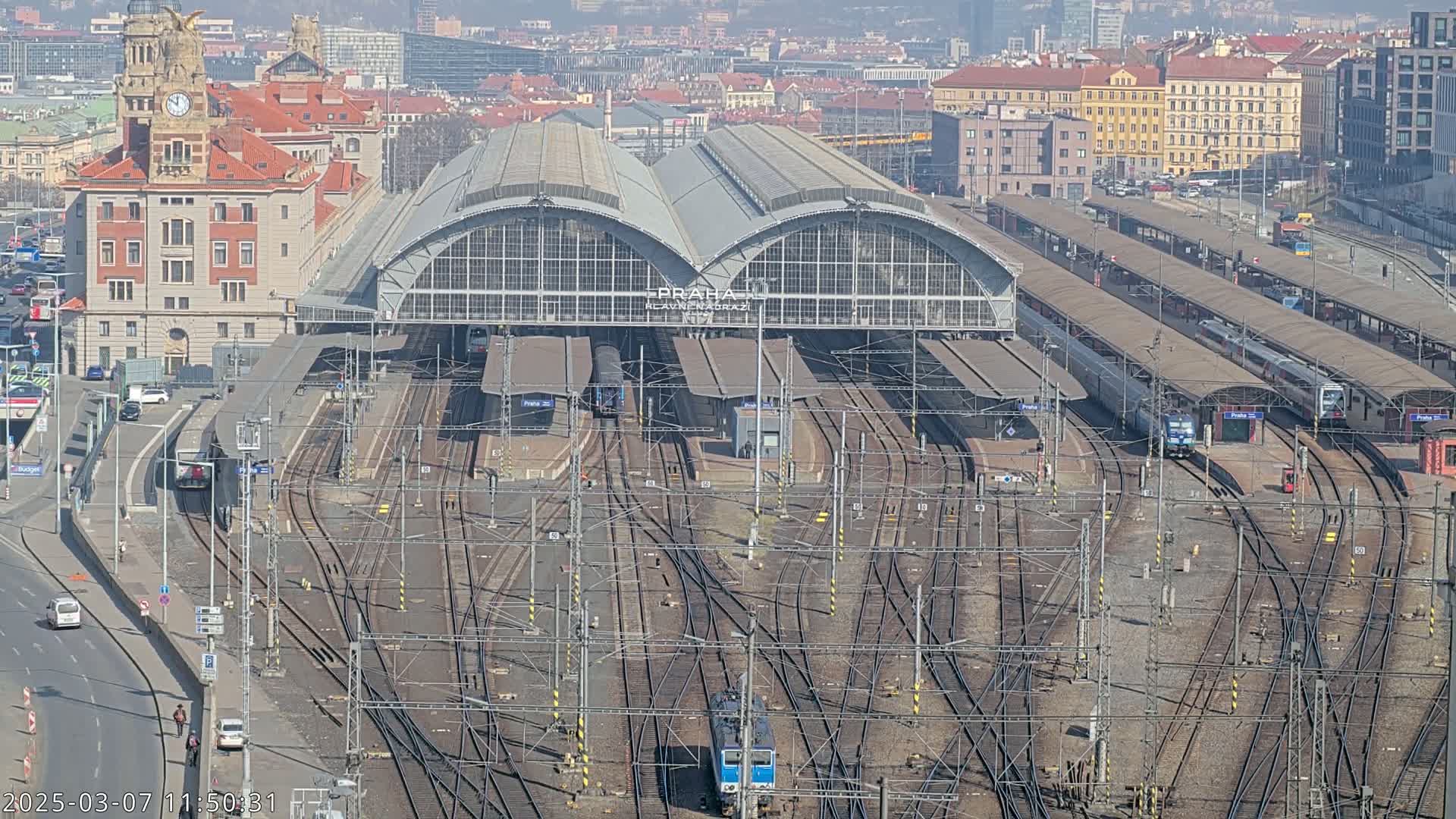 A large train station with numerous tracks and trains, under a sunny sky.