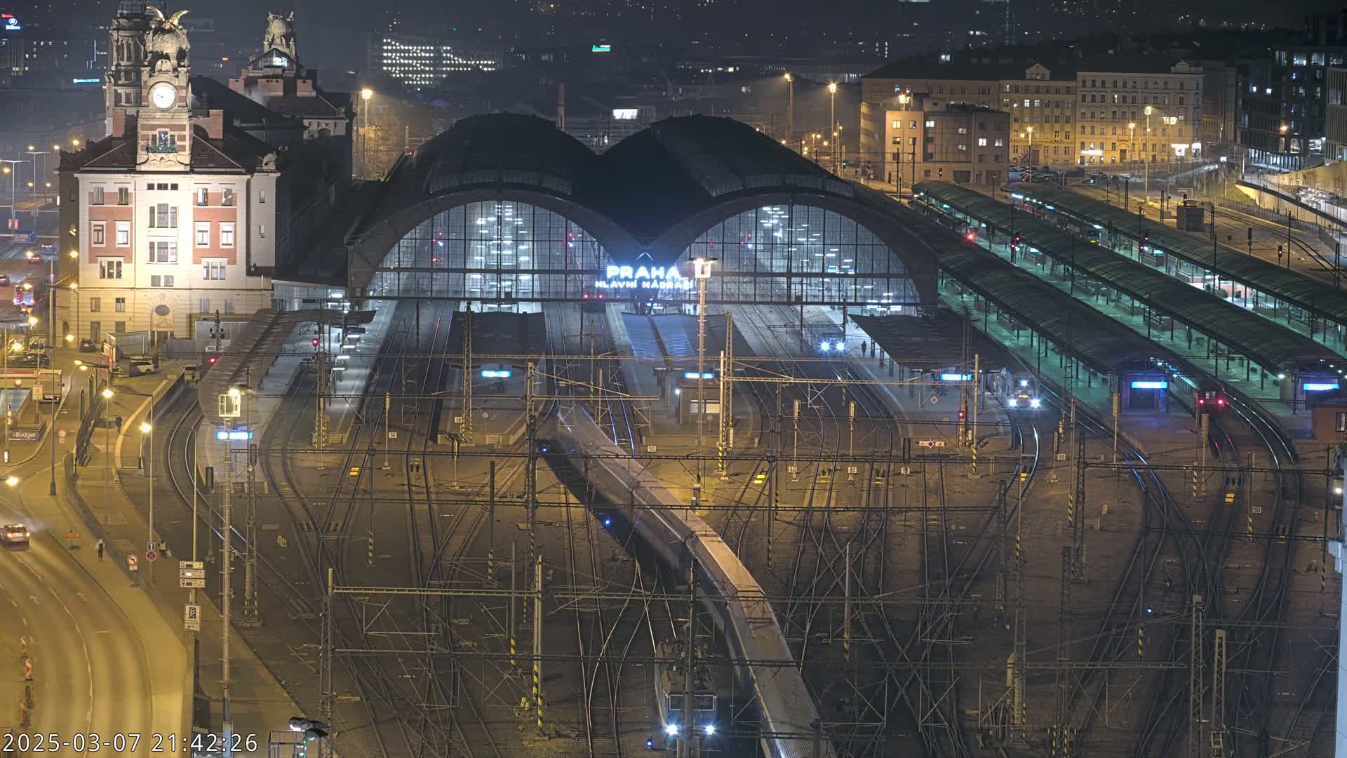 A nighttime aerial view of a large train station with many tracks and platforms, illuminated by artificial lights.