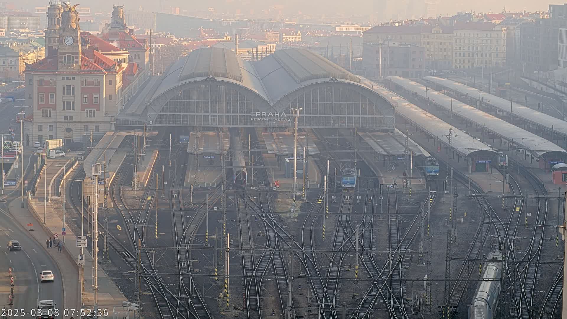 A large train station with numerous tracks and platforms, surrounded by city buildings, on a hazy day.