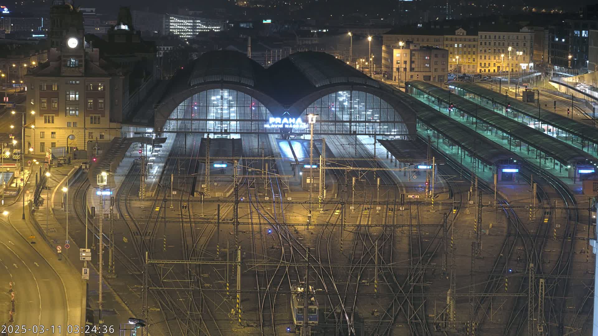 A brightly lit, large train station at night with many tracks and platforms extending outward.