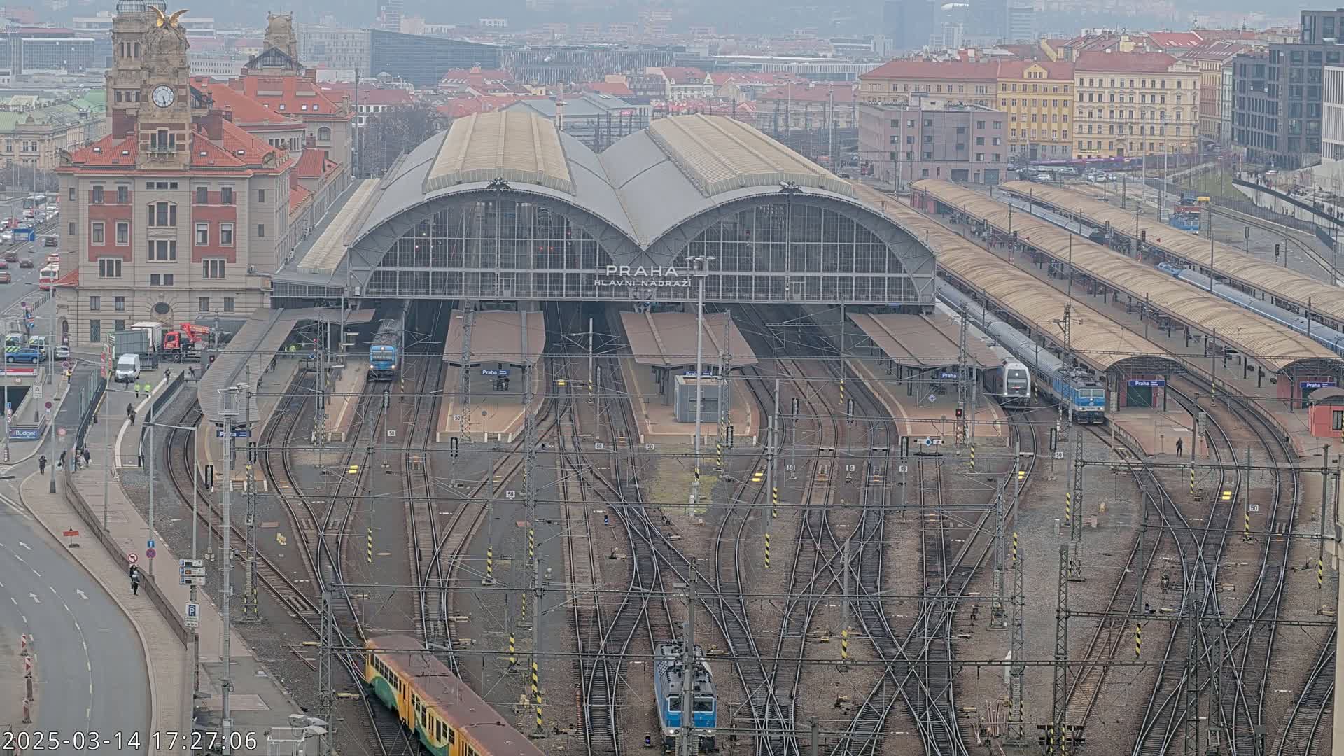 A large train station with numerous tracks and trains, surrounded by city buildings, on an overcast day.
