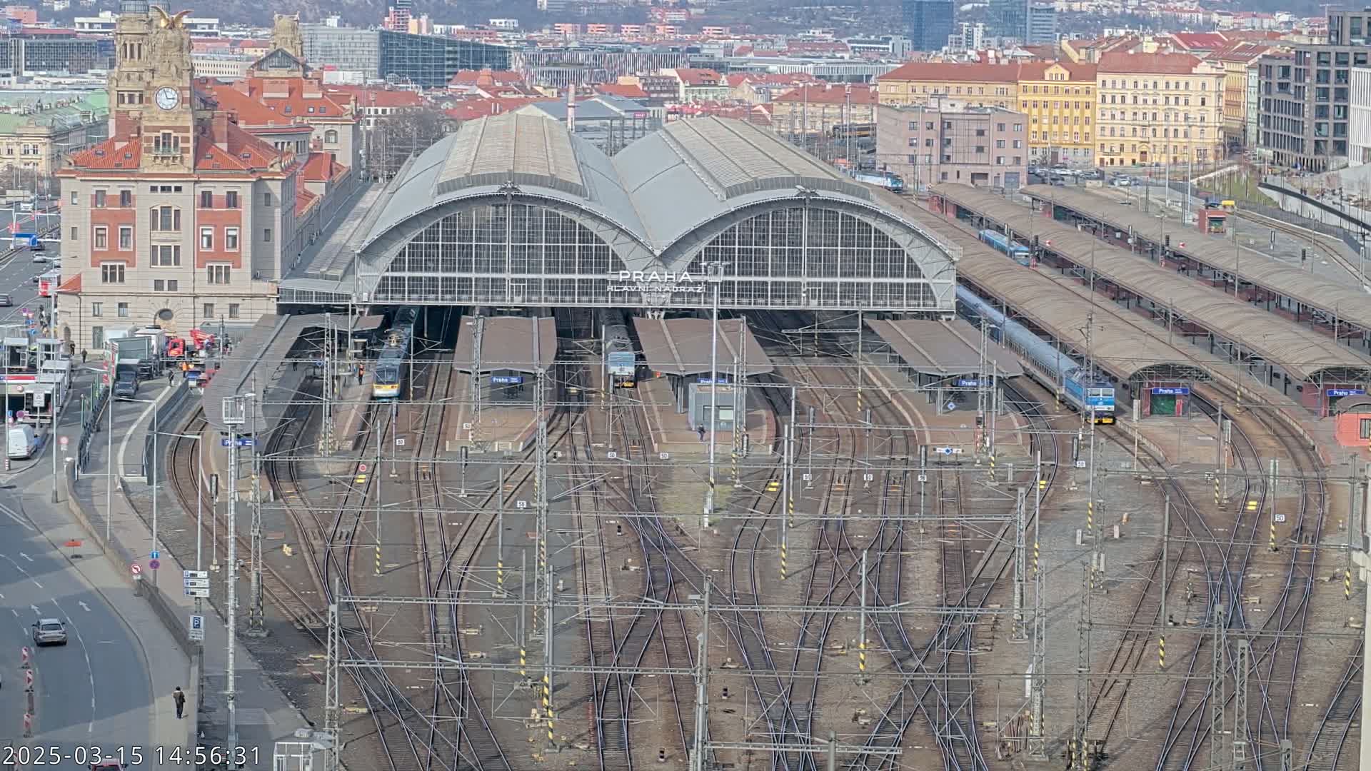 A large train station with multiple trains and a complex network of tracks is viewed from above on a clear day.