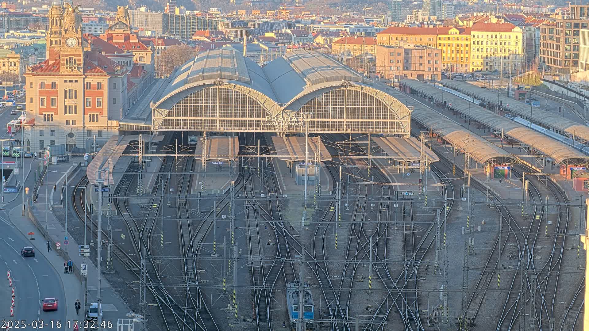 A large train station with many tracks and platforms is seen from above on a sunny day.