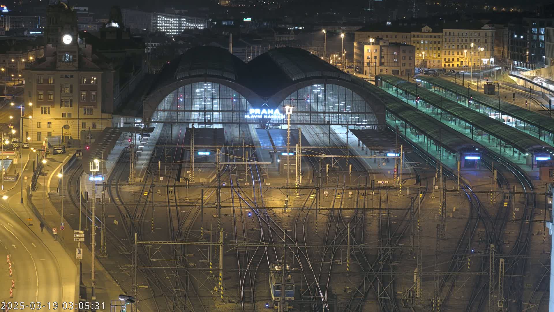 A brightly lit train station at night, surrounded by a complex network of train tracks and platforms.
