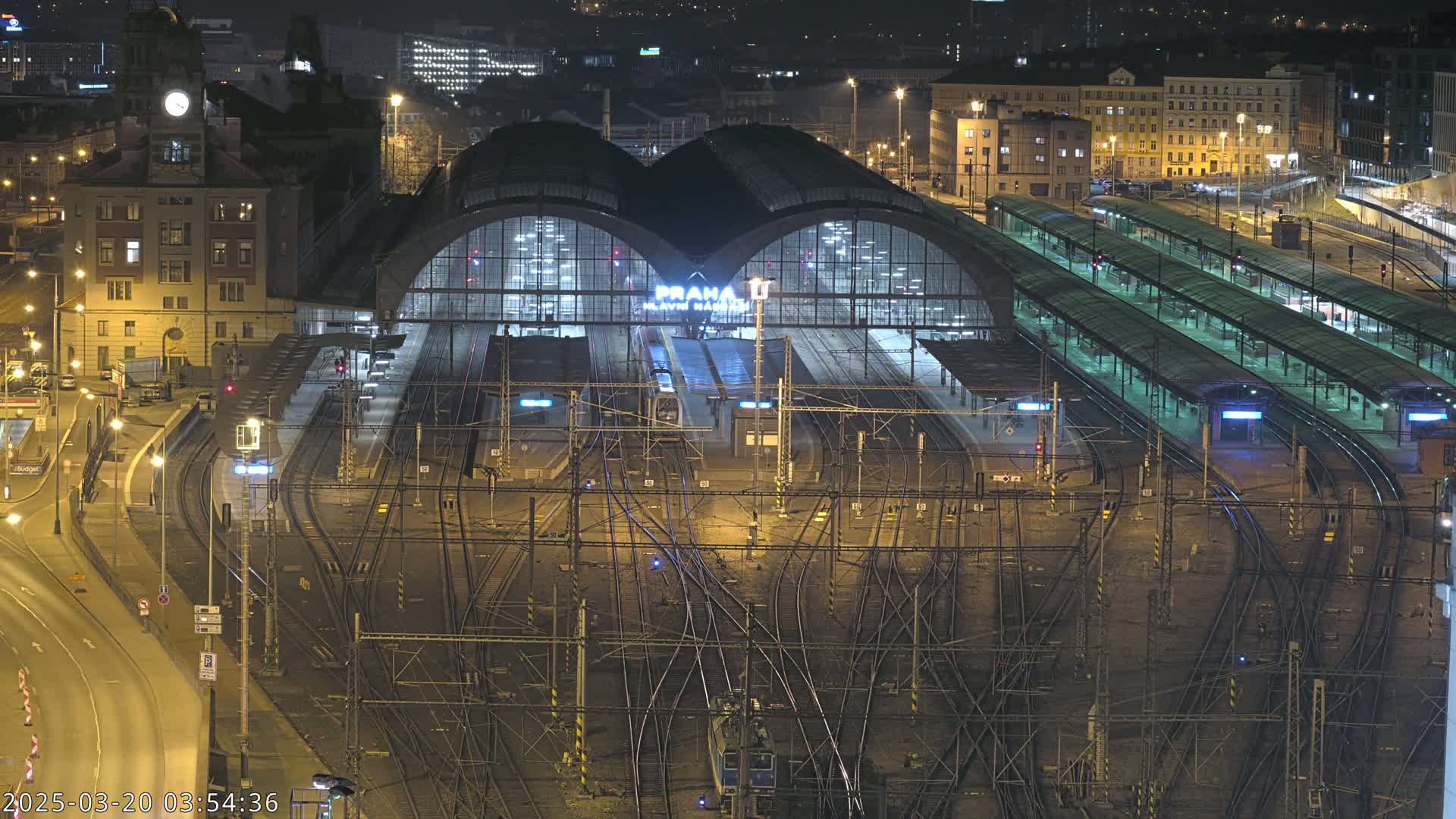 A nighttime aerial view of a large, illuminated train station with numerous tracks and platforms.