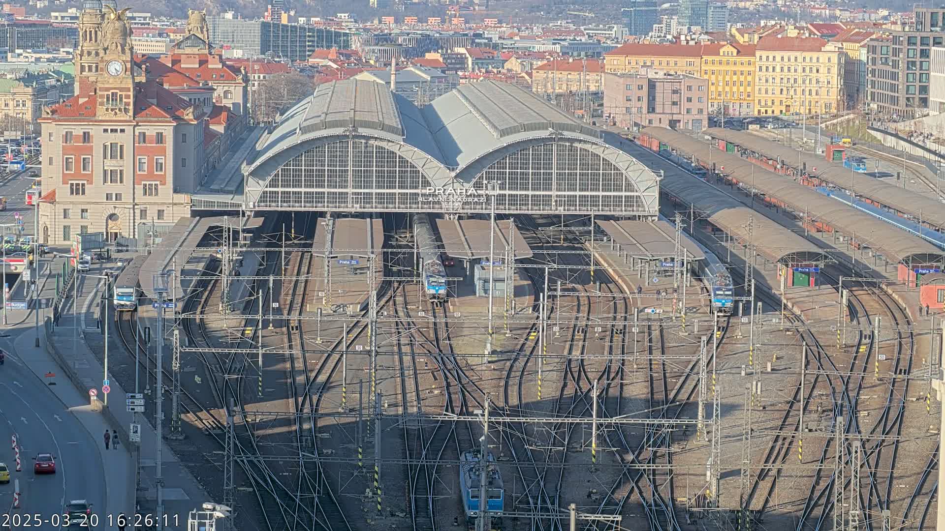 A large train station with multiple tracks and several trains, situated in a city on a sunny day.