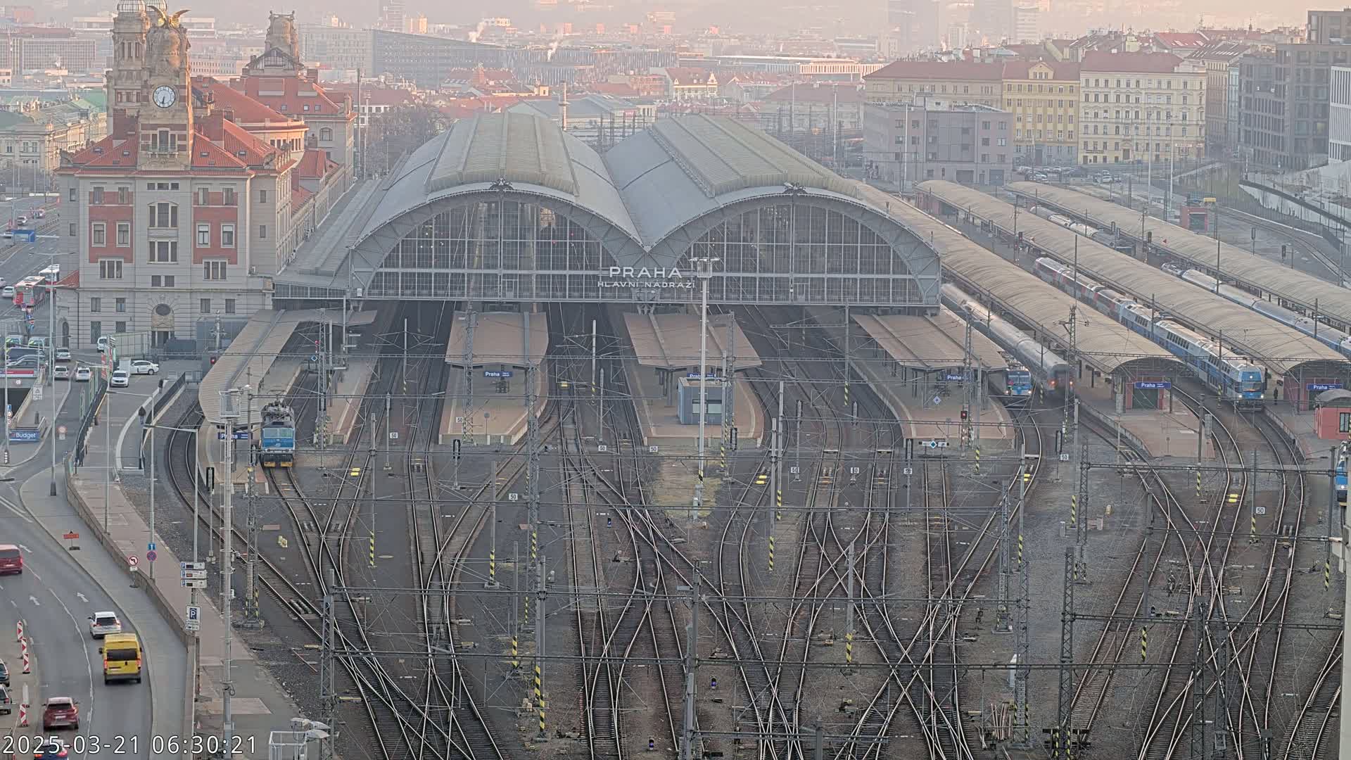 A large train station with numerous tracks and trains, under a hazy sky.