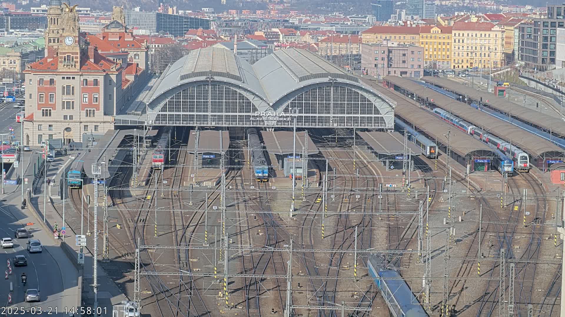 A large train station with numerous trains and tracks, situated in a city on a sunny day.