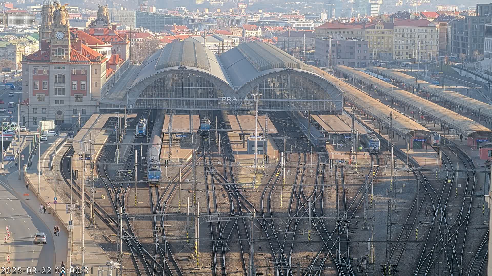 A large train station with numerous tracks and trains, viewed from above on a sunny day.