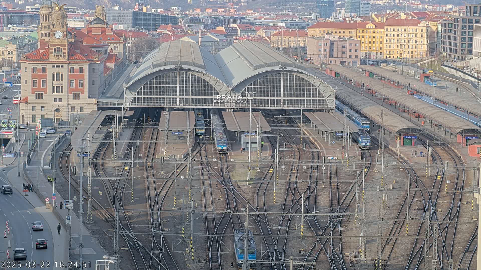 A large train station with numerous tracks and trains, surrounded by city buildings, on a clear day.