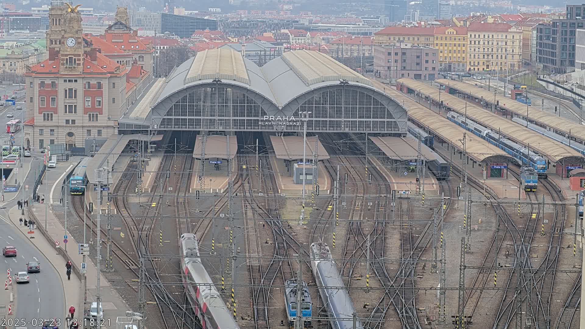 An aerial view of a large train station with numerous tracks, trains, and platforms, on an overcast day.