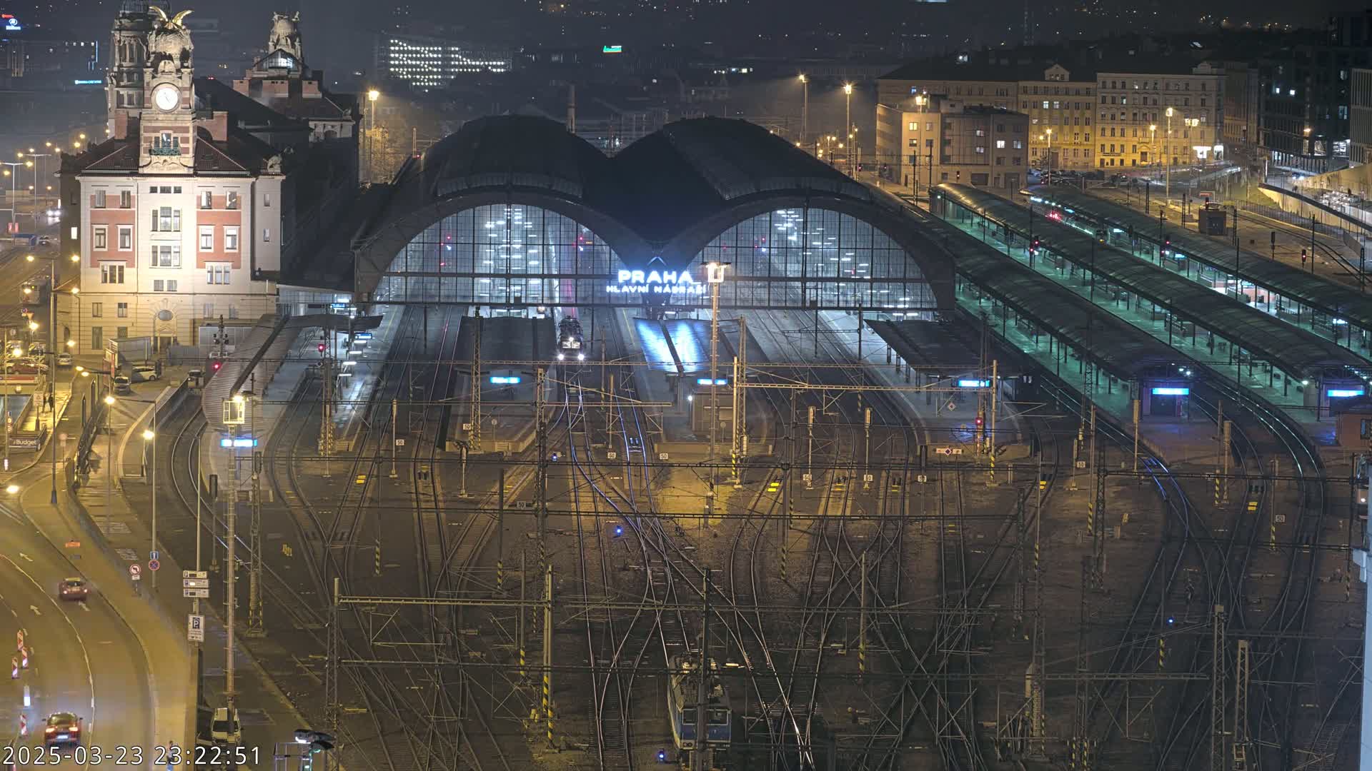 A large, illuminated train station at night, with many train tracks and platforms, and a building with a clock tower.